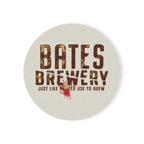 A round ceramic coaster featuring the Bates Brewery logo and tagline “Beer Like Mother Used to Brew”, displayed on a wooden table.